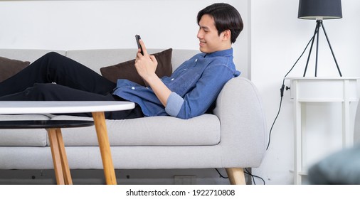 Young Asian Man Lying On Sofa And Using Phone
