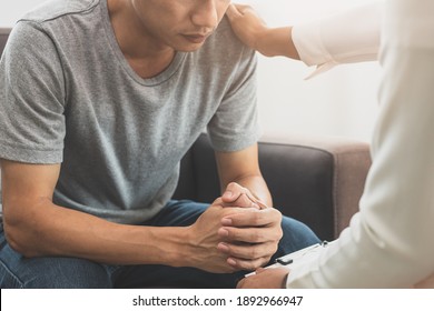 Young asian man, male suffers from a mental who needs to therapy with a psychologist while sitting on couch to consult, psychiatrist has encouragement the patient by touching to make his feel relaxed. - Shutterstock ID 1892966947