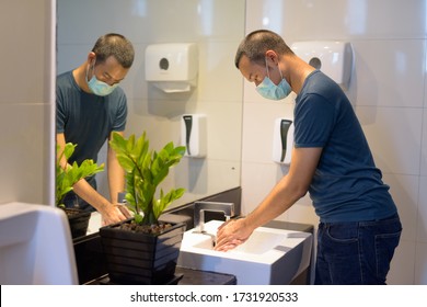 Young Asian Man With Mask Washing Hands As Proper Hygiene Etiquette In The Bathroom