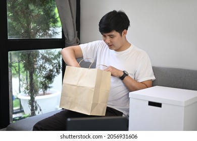 Young Asian Man Opening Gift In Living Room.