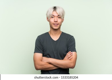 Young asian man over isolated green background keeping the arms crossed in frontal position