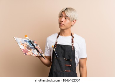 Young asian man over isolated background holding a palette and thinking an idea