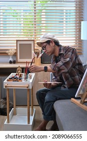 Young Asian Man Painting Picture With Water Color In Living Room.