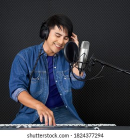 Young asian man playing an electric keyboard in front of black soundproofing walls. Musicians producing music in professional recording studio.