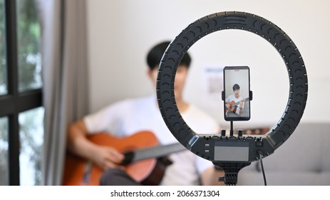 Young Asian Man Playing Guitar And Streaming Online Vlog With Smart Phone At Home.