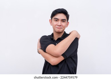 A young asian man pouts while embracing himself while feeling content. Deserving self-love concept. Isolated on a white backdrop. - Shutterstock ID 2244759579