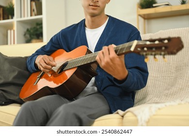 Young asian man practicing acoustic guitar in a cozy living room - Powered by Shutterstock