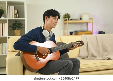 Young asian man practicing acoustic guitar in a cozy living room - Powered by Shutterstock