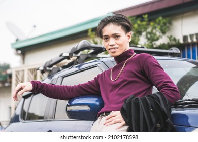 A Young Asian Man In A Purple Sweater And A Big Gold Chain Necklace Posing In Front Of His Blue Car.