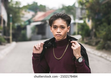 A Young Asian Man In A Purple Turtle Neck Sweater And A Big Gold Chain Necklace Standing In Front Of A Road.