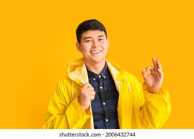 Young Asian Man In Raincoat Showing OK On Color Background