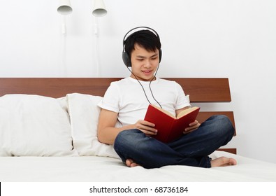 A Young Asian Man Reading A Book On A Bed