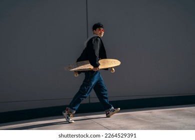 young asian man with red glasses walking happy with surf skate in hand urban lifestyle - Powered by Shutterstock