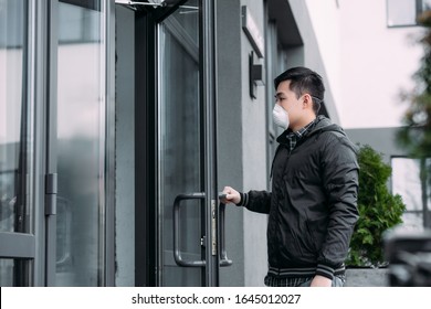 Young Asian Man In Respirator Mask Opening Door And Entering Building