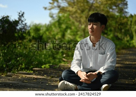 Young Asian man resting and contemplating sitting in the outdoor park.