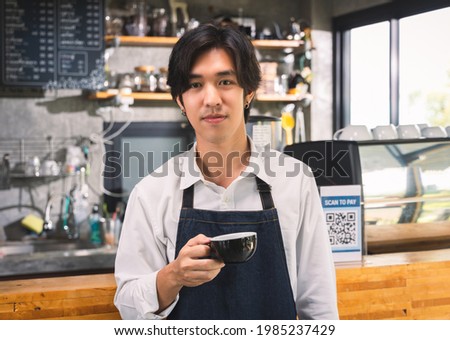 Young asian man servings cup of hot coffee latte standing at counter in coffee cafe shop.