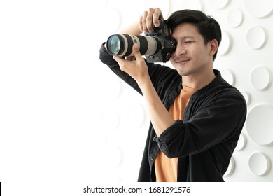 Young Asian Man Shooting Photo By Digital Camera In Photography Studio. Portrait Of Male Photographer Taking Pictures. Camera Shooting Is Happy Hobby. Behind The Scene Of Journalist Takes Photographs.