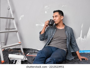 A young Asian man sips coffee while taking a break from home improvement DIY - Powered by Shutterstock