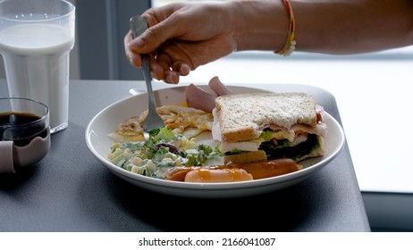 A Young Asian Man Sits At The Dining Room Table Full Of Food, He Dunks The Food On The Plate And Eats It, Relishing It.