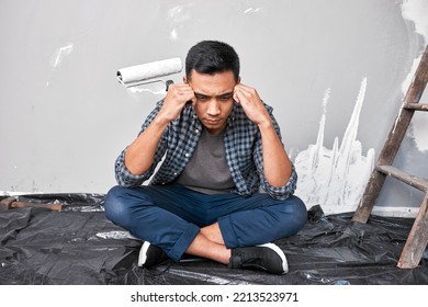 A Young Asian Man Sits With Head In Hands Overwhelmed By Home DIY Project