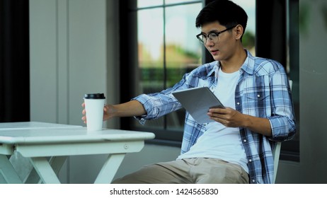 Young asian man sitting on chair, he use tablet in hand and drinking beverage together copy space for insert text - Powered by Shutterstock