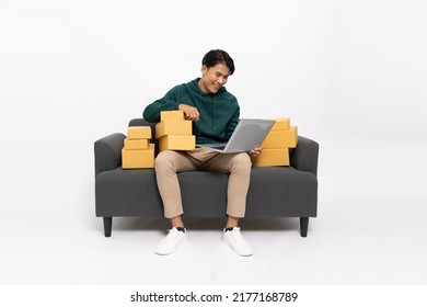 Young Asian man sitting on sofa with laptop computer and package parcel box isolated on white background, Delivery courier and shipping service concept