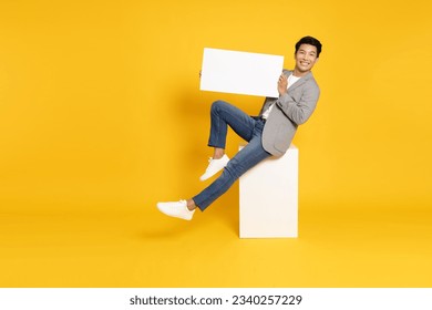 Young Asian man sitting and showing blank white billboard isolated on yellow background - Powered by Shutterstock