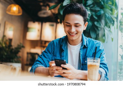 Young Asian man sitting and using smartphone at coffee shop - Powered by Shutterstock