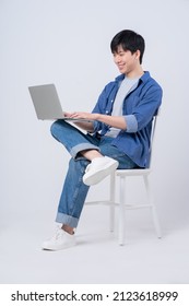 Young Asian man sitting and using laptop on white background - Shutterstock ID 2123618999