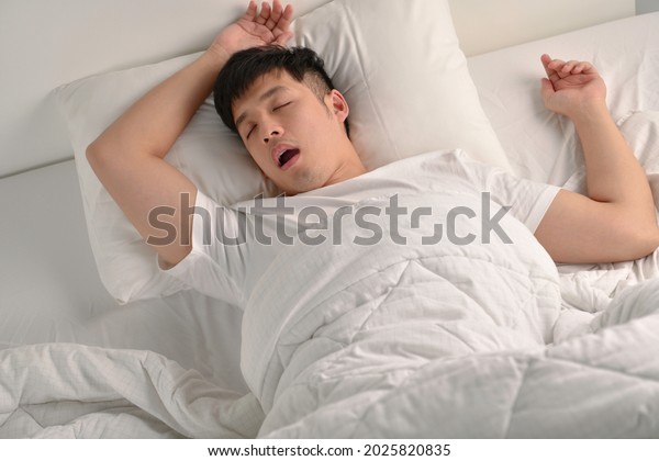 Young Asian man sleeping and snoring loudly lying\
in the bed\
