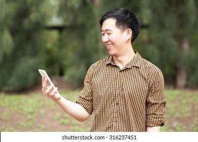 Young Asian man smiling with his phone on his hand.