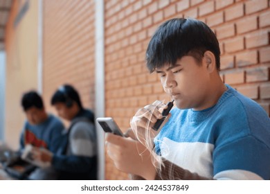 Young asian man smoking electronic cigarette and using mobile phone in front of brick wall. - Powered by Shutterstock