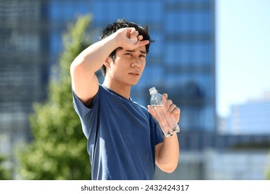 Young Asian man in sportswear hydrating with plastic bottle outdoors - Powered by Shutterstock