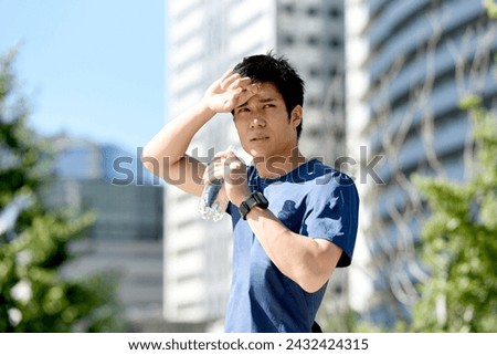 Young Asian man in sportswear hydrating with plastic bottle outdoors