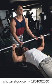 A Young Asian Man Spots An Older, More Experienced Guy While Doing Bench Presses. Chest Workout At The Gym.