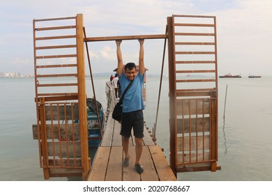 A young Asian man standing arms up in an open lattice door on a narrow wooden pier with view on the harbor from Georgetown, Malaysia 
