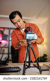 Young Asian Man Standing Behind Camera And Adjusting Camera Settings To Record Video Blog At Home