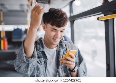 Young Asian Man Is Standing In The Bus Using Phone And Holding Onto The Bar While Waiting To Arrive At Her Destination.