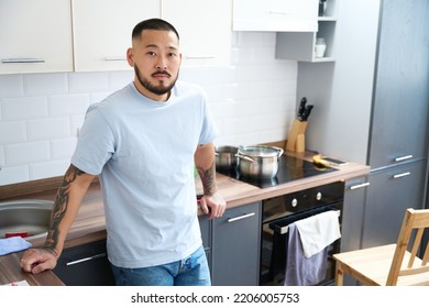 Young Asian Man Standing By The Kitchen Cabinet