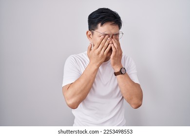 Young asian man standing over white background rubbing eyes for fatigue and headache, sleepy and tired expression. vision problem 