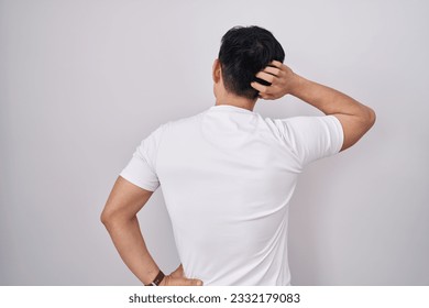 Young asian man standing over white background backwards thinking about doubt with hand on head  - Powered by Shutterstock