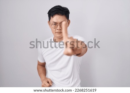 Young asian man standing over white background pointing with finger up and angry expression, showing no gesture 