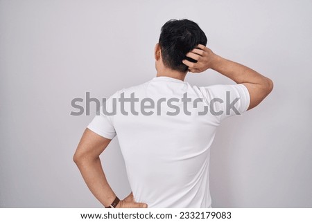 Young asian man standing over white background backwards thinking about doubt with hand on head 