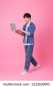 Young Asian Man Standing And Using Laptop On Pink Background