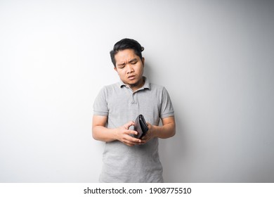 Young Asian man, stressful face expression when looking in empty wallet, economy problem, bankruptcy or broke concept, isolated portrait, selective focus