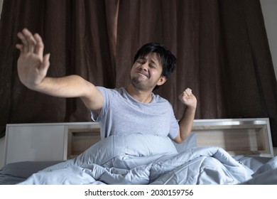 young asian man stretching in bed in the morning after wake up