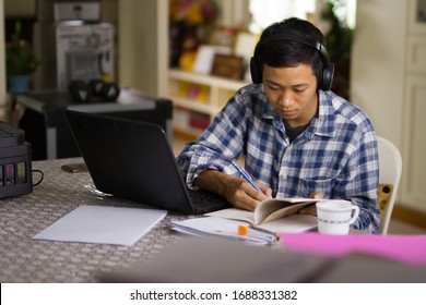 Young Asian Man Student Study Online Class At Home With Serious Face While Looking At Laptop And Writing A Notebook.