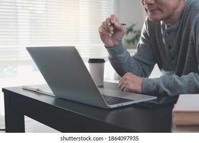 Young Asian Man Student Watching Video Channel Tutorial Via Laptop Computer, Studying Online Class. Business Man Making Facetime Video Conference Using Zoom Online Meeting App, Work From Home Concept 