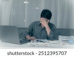 Young Asian man suffering from pain from working at desk, feeling tired from working on laptop and financial documents in office for a long time, Conceptual Office Syndrome