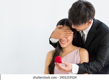 Young Asian Man Surprise Girlfriend Amd Propose To Her With Ring On White Background. Couple Togther And Valentines Concept